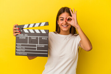 Young caucasian woman holding clapperboard isolated on white background excited keeping ok gesture on eye.