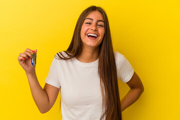 Young caucasian woman holding a home keys isolated on yellow background laughing and having fun.