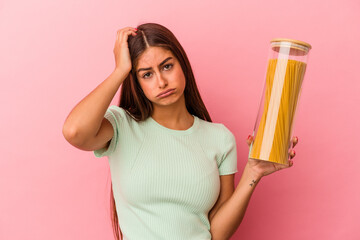 Obraz premium Young caucasian woman holding a pasta jar isolated on pink background being shocked, she has remembered important meeting.