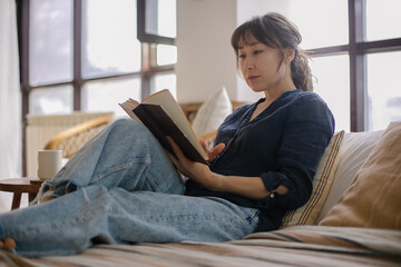 Young asian woman reading the book on bed at home. Concepts of home and comfort - 442134138