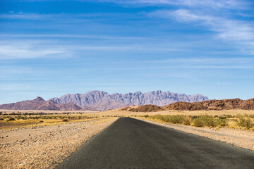 Namib desert in Sossusvlei in daylight. Naukluft mountains and tarred road under the blue sky.