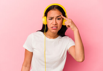 Young Venezuelan woman listening to music isolated on pink background showing a disappointment...