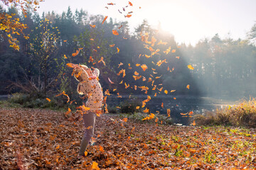 Smiling girl child throwing dry leaves in the air at beautiful autumn sunset.