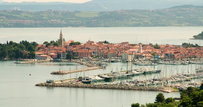 Elevated view of old town Izola in Slovenia. Adriatic Sea coast. Boats and yachts docket in marina. Panoramic static shot of Mediterranean settlement Isola. Sailboat leave the harbor. Zoom in