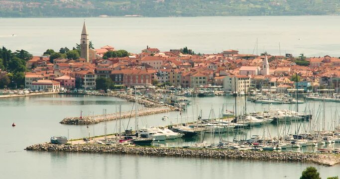 Elevated view of old town Izola in Slovenia. Adriatic Sea coast. Boats and yachts docket in marina. Panoramic static shot of Mediterranean settlement Isola. Sailboat leave the harbor. Left tracking