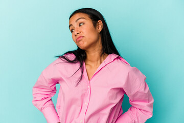 Young Venezuelan woman isolated on blue background shrugs shoulders and open eyes confused.