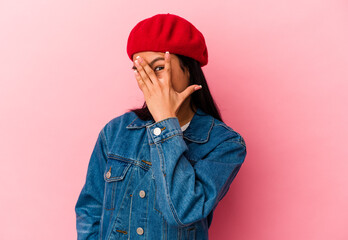 Young Venezuelan woman isolated on pink background blink at the camera through fingers, embarrassed covering face.