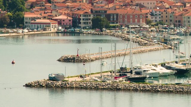 Elevated view of old town Izola in Slovenia. Adriatic Sea coast. Boats and yachts docket in marina. Panoramic static shot of Mediterranean settlement Isola. Sailboat leave the harbor. Left tracking