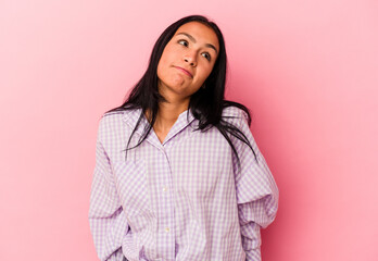 Young Venezuelan woman isolated on pink background shrugs shoulders and open eyes confused.