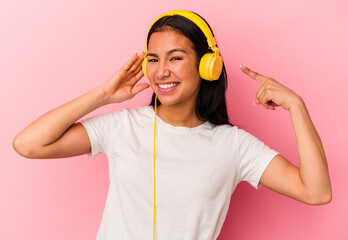 Young Venezuelan woman listening to music isolated on pink background