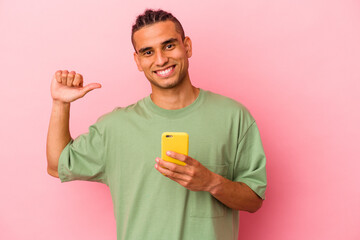 Young Venezuelan man holding a mobile phone isolated on pink background feels proud and self confident, example to follow.