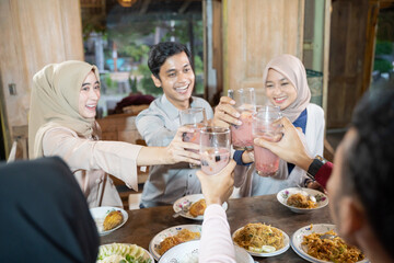 group of young asian people celebrating and raising glasses of fruit ice for toast while breaking fast together in the dining room