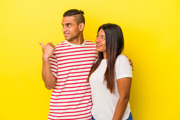 Naklejka premium Young latin couple isolated on yellow background points with thumb finger away, laughing and carefree.