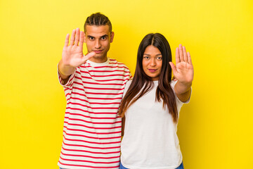 Young latin couple isolated on yellow background standing with outstretched hand showing stop sign,...