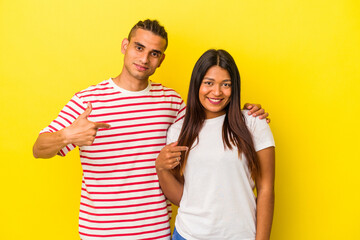 Fototapeta premium Young latin couple isolated on yellow background person pointing by hand to a shirt copy space, proud and confident