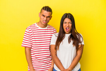 Young latin couple isolated on yellow background screaming very angry and aggressive.
