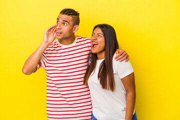 Young latin couple isolated on yellow background shouting and holding palm near opened mouth.