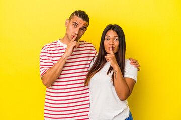 Naklejka premium Young latin couple isolated on yellow background keeping a secret or asking for silence.