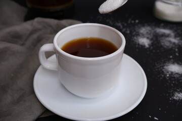Cup of black coffee with sugar on a black background