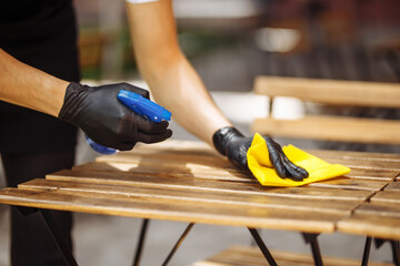 Close-up shot of a waiter in black gloves with a disinfectant in his hands, wiping the furniture before opening it. Disinfection with a special agent against virus, microbes, infection.