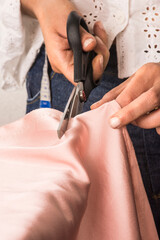 Woman cutting a pink satin dress with scissors to later sew