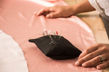Woman's hands on a pink silk fabric preparing a dress for sewing