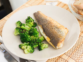fried fillet of sea bass with garnish of broccoli on black warm stone plate