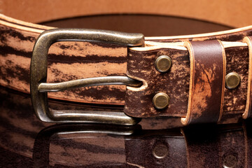 Brown leather belt with scuffs and a metal buckle on a dark background.