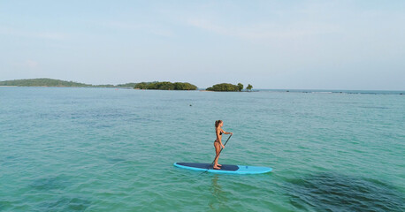 Aerial drone bird's eye view of man exercising sup paddle board in turquoise tropical clear waters, Thailand