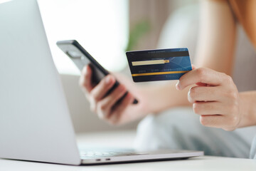 Young woman holding credit card and using smart phone for online shopping, internet banking, e-commerce, spending money, working from home concept