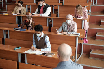 Group of students making notes by desks at lecture