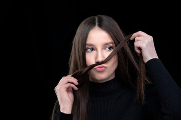 Obraz premium A beautiful girl with long hair fooling around in front of the camera. Makes a mustache out of hair.