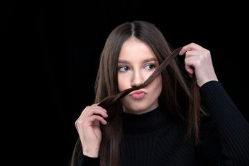 A beautiful girl with long hair fooling around in front of the camera. Makes a mustache out of hair.