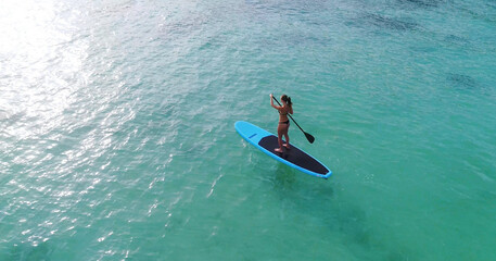 Aerial drone bird's eye view of man exercising sup paddle board in turquoise tropical clear waters,...