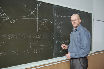 Serious professor explaining algebraic formula by blackboard © pressmaster