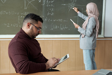 Young student in hijab and her teacher by blackboard