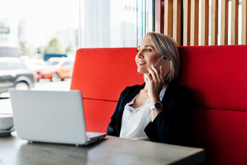 Obraz premium An attractive girl is talking on a mobile phone and smiling, sitting alone in a cafe