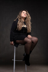 Fototapeta premium Beautiful fat woman with long curly hair in black clothes on a gray background. Plus size model girl.