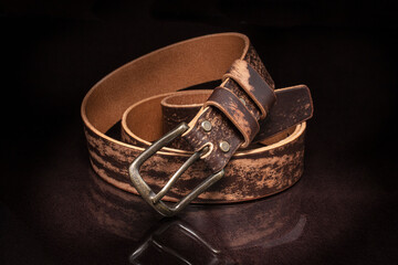 Brown leather belt with scuffs and a metal buckle on a dark background.
