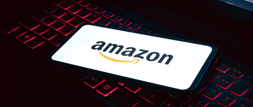  Amazon. A logo da Amazon na tela de um celular que est&aacute; sobre um teclado de notebook com ilumina&ccedil;&atilde;o de leds. Fotografia em ambiente noturno. Site, Com&eacute;rcio eletr&ocirc;nico, online, Venda, Varejo, produto.
