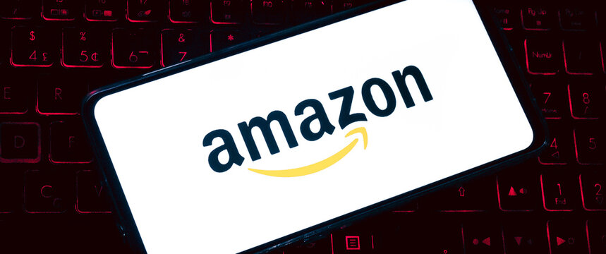  Amazon. A logo da Amazon na tela de um celular que est&aacute; sobre um teclado de notebook com ilumina&ccedil;&atilde;o de leds. Fotografia em ambiente noturno. Site, Com&eacute;rcio eletr&ocirc;nico, online, Venda, Varejo, produto.