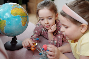 Two cute little girls playing with toy planets at home