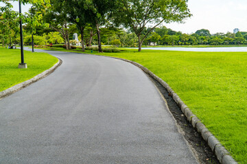 Beautiful green city park with blue sky. Pathway and beautiful trees track for running or walking and cycling relax in the park on green grass field on the side. Sunlight and flare background concept.