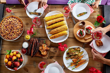 Top view over a dining table, decorated with flowers, with tableware and food. Backyard picnic with friends or neighbors, family dinner.