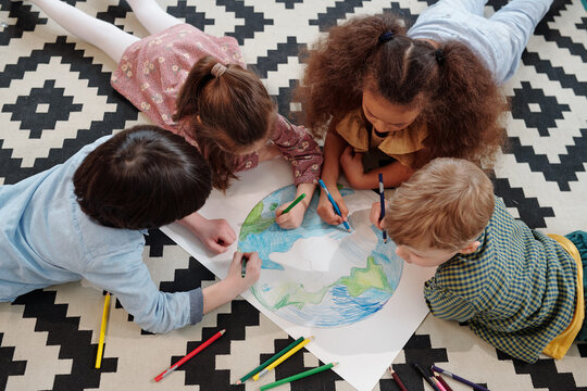 Cute kids drawing planet on large paper while lying on the floor