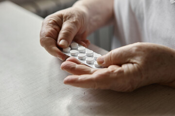 Sad old woman taking pills, health problems in old age, expensive medications. An elderly woman's hands unpacking several pills for taking medication. Grandma takes tablet and drinks a glass of water