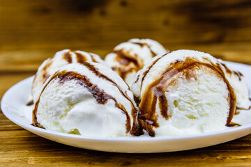 Plate with ice cream balls and chocolate topping on a wooden table