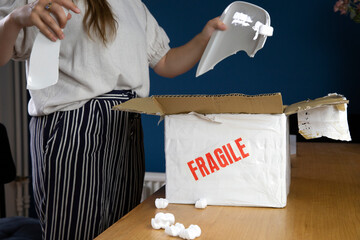 Young woman opening damaged delivery package,online shopping package. Broken fragile plate at home