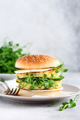 Burger healthy vegetarian with egg and pea shoots and seeds microgreen, fresh salad, cucumber slice on a cutting wooden board on light background. Selective focus