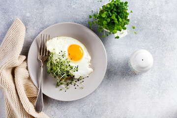 Fried eggs with arugula microgreen in gray ceramic plate on gray concrete old background. Traditional English breakfast. Top view